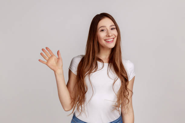 mujer feliz de pie con la mano levantada saludando a la cámara, saludando a los invitados con una sonrisa amistosa. - waving arms fotografías e imágenes de stock