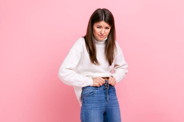 portrait of unhappy sad young adult woman gaining weight, cant wearing her jeans, being overweight. - torso women jeans abdomen imagens e fotografias de stock