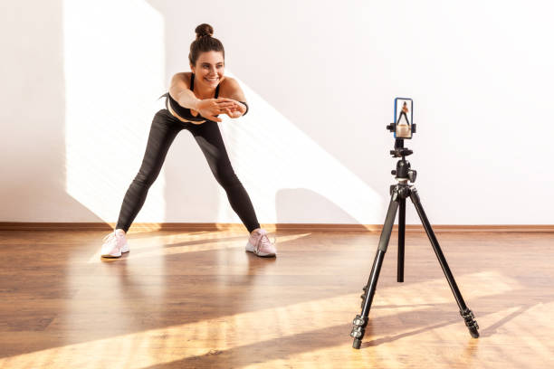 istock Attractive trainer broadcasting online stretching class, recording video via cell phone on tripod. 1358640186