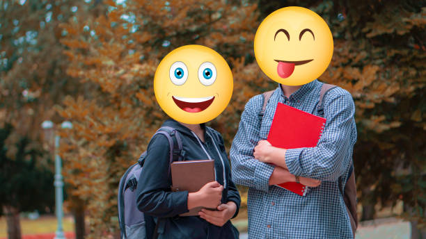 istock Two young students posing outside with notebooks. They are unrecognizable because they have emojis on their face.It is unclear who they are. The background shows that it is autumn. Trees with yellowed leaves appear. 1358641953