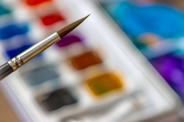 Colorful squares of watercolor paint on a palette with a small art brush. Selective focus.
