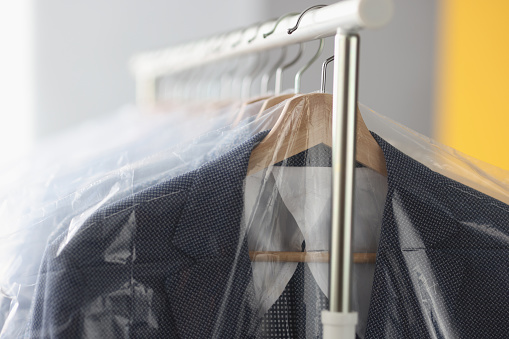 Clothes in plastic bags hanging on hanger in laundry closeup. Dry cleaning service concept