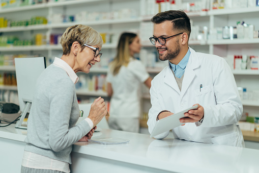 Farmacéutico joven que da medicamentos recetados a una clienta mayor en una farmacia photo
