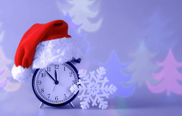 istock Alarm clock in red Santa hat, white snowflake, silhouettes Christmas tree on abstract background. 1358658101