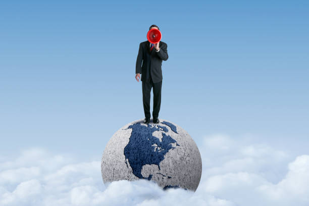 istock Man Standing On Globe Shouts Through A Megaphone 1358667491