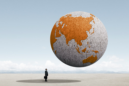 A businessman holding a briefcase looks up as he stands in the shadow cast by a large globe rotated toward the Asian continent. The file was created using Adobe Photoshop.  Map source: https://eclipse.gsfc.nasa.gov/transit/TV2004/Earth-Ingress1a.JPG