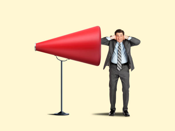 istock Man Placing His Hands Over His Ears Stands In Front Of Large Megaphone 1358671132