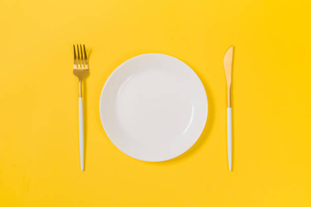 istock empty white plate with fork and knife isolated on yellow background 1358675594