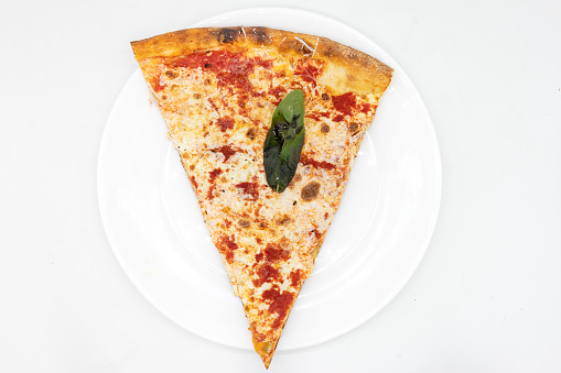 An overhead view of a New York City style margherita pizza slice on a white plate over a white background