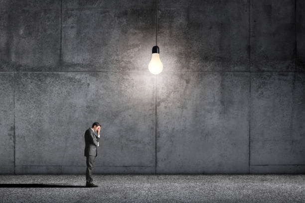 istock Man Standing In Large Room Illuminated By Single Light Bulb 1358683170