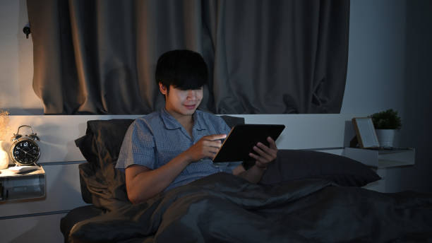 istock Asian man sitting in bedroom and browsing internet with digital tablet. 1358691612