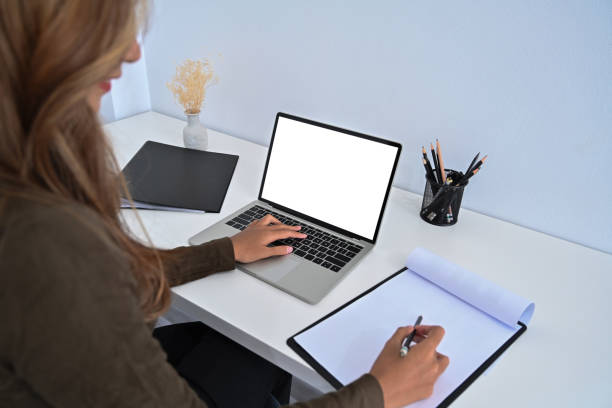 istock Cropped shot businesswoman using laptop computer and writing information on paperwork. 1358692064