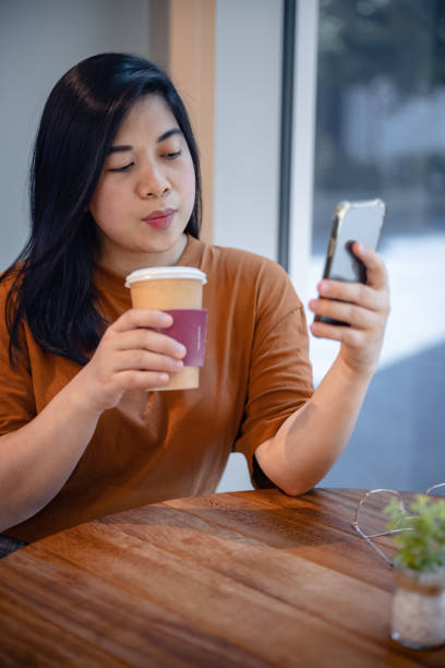 istock Young woman using mobile phone for video call in cafeteria 1358700838