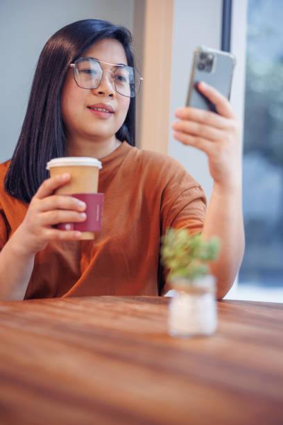 istock Smiling young woman using mobile phone for video call in cafeteria 1358700875