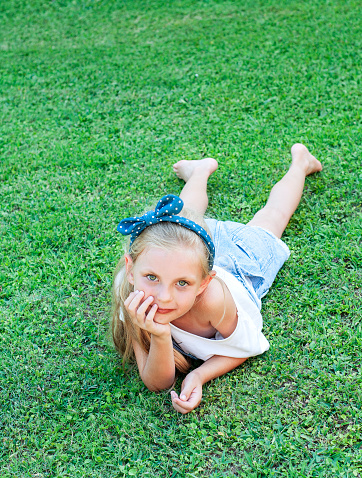 Ð¡heerful little girl in a denim jumpsuit, lying on a green grass