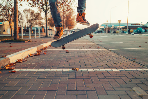 Skateboarding. A man does an Ollie stunt on a skateboard. Board in the air. Close-up of legs. Street on the background.
