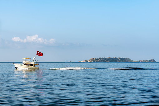 A small motor boat with a Turkish flag advancing fast. The island of Kastellorizo (Megisti, Meis) is visible in the background.