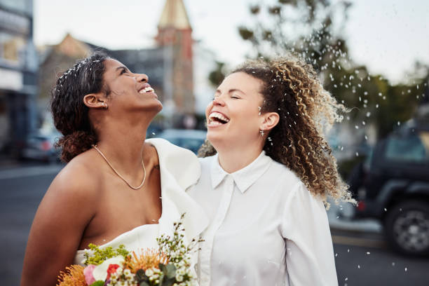 Shot of a young lesbian couple standing outside together and celebrating their wedding Love conquers all wedding stock pictures, royalty-free photos & images