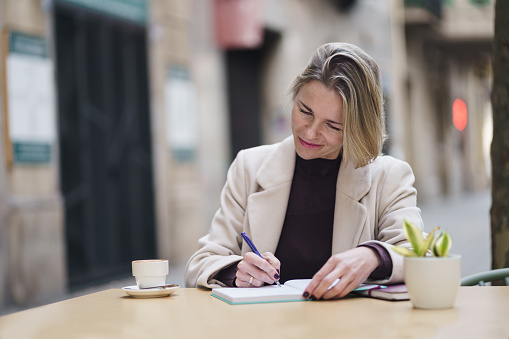 Confident elegant woman sitting at coffee shop and writing ideas and inspiration in her notebook
