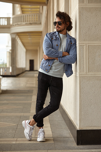 a stylish guy with glasses stone wall on the background and looks away. strong and strict male. in casual clothes.