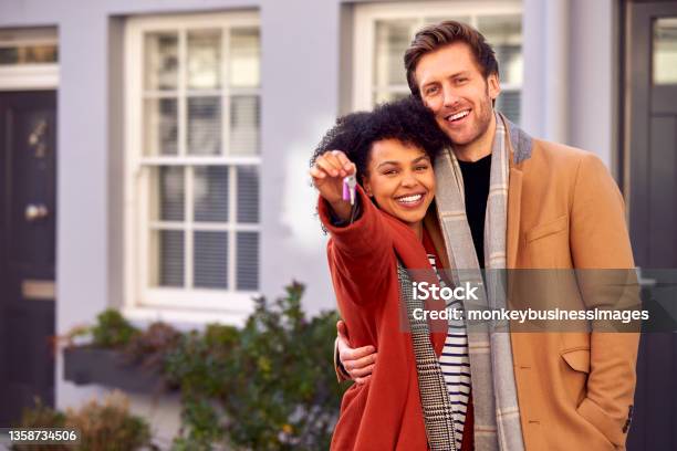 Portrait Of Multi Cultural Couple Outdoors On Moving Day Holding Keys To New Home In Fall Or Winter Stock Photo - Download Image Now