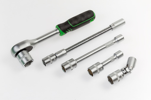 Ratchet wrench, two straight extensions of different lengths, gimbal joint and long flexible adapter with inserted interchangeable hexagonal sockets lie on a light surface