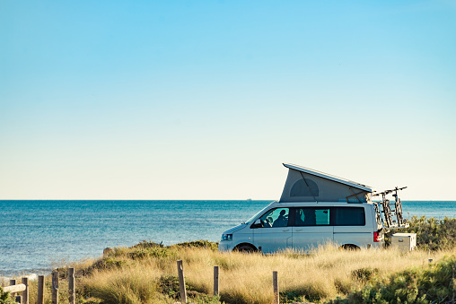 Camper van with roof top tent camping on mediterranean sea coast. Holidays and travel in motorhome.
