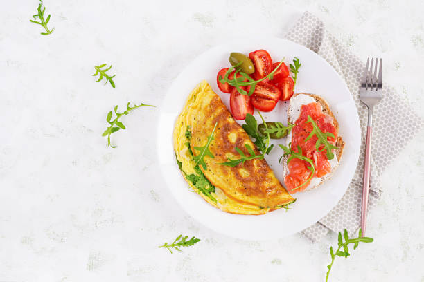 istock Breakfast. Omelette with cheese, green arugula and sandwich with salmon on white plate.  Frittata - italian omelet. Top view 1358739256
