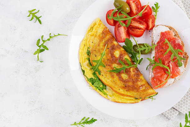 istock Breakfast. Omelette with cheese, green arugula and sandwich with salmon on white plate.  Frittata - italian omelet. Top view 1358739265