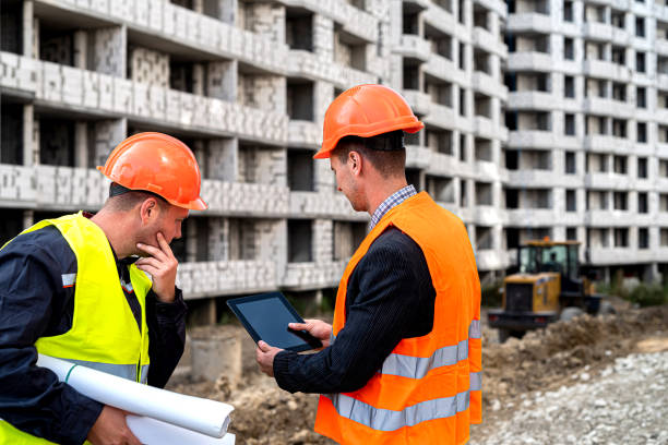 istock young strong hardy construction workers in overalls standing near a new building with a plan 1358740121
