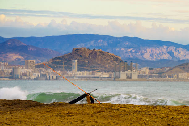 Fishing rod on beach sea shore. Alicante city in the distance. Spain, Costa Blanca.