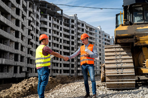 istock two good workers in uniform shake hands near the grader and the new building 1358740778