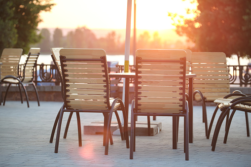 Closeup of outdoors cafe chairs and table at sunset on city street.