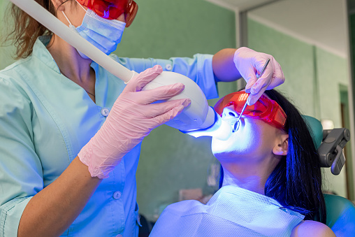 Woman in dentistry making whitening procedure with stomatologist