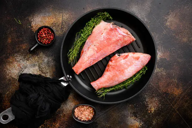 Photo of Red sea perch raw whole fresh fish, in frying cast iron pan, on old dark rustic table background, top view flat lay, with copy space for text