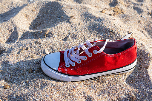 One red sneaker shoe on sand beach background