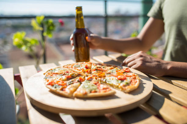 Close-up of pizza and beer bottle on table. Male hand holding bottle over table with pizza slices. Food, menu, cafe concept