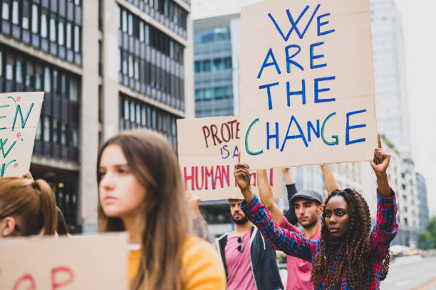 pessoas greve contra as mudanças climáticas e poluição, jovem mulher africana segurando um cartaz comunicando que somos a mudança - placa de manifestação - fotografias e filmes do acervo