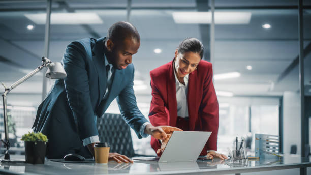 istock Company CEO and Top Manager Talking, Using Laptop Computer while in Big City Office. Strategy Meeting of Two Businesspeople Brainstorming Business Idea of e-Commerce Software Investment 1358748474
