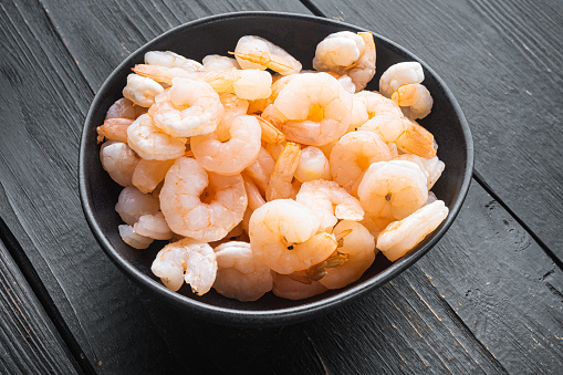 Pile of boiled peeled  shrimps set, in bowl, on black wooden table