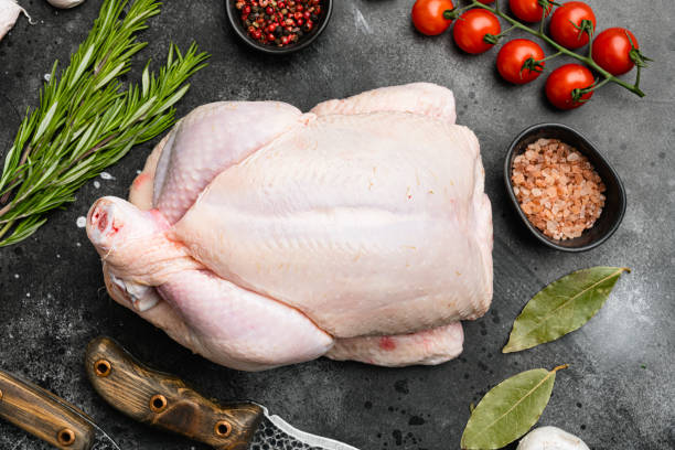 Organic raw whole chicken, on black dark stone table background, top view flat lay