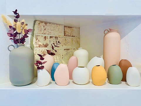Horizontal still life close up of variety of hand made pastel color ceramic vase with against white and brick shelf