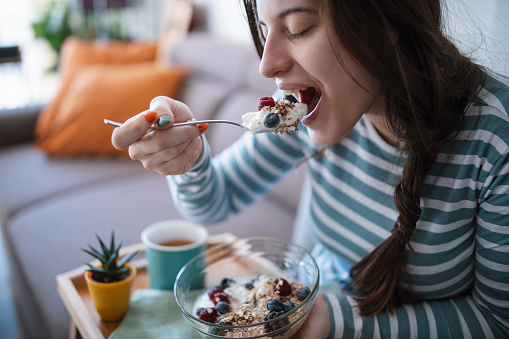 Young cheerful woman eating healthy and delicious breakfast in sunny morning
