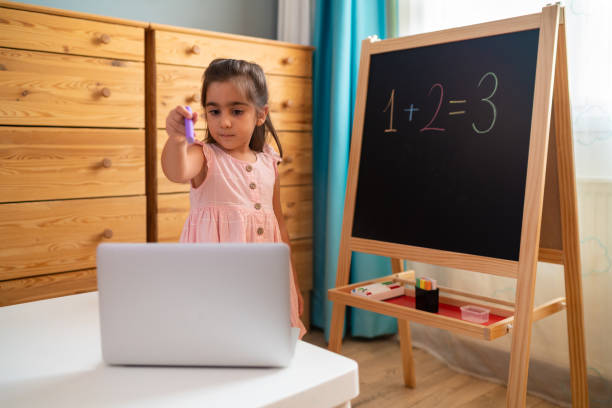 маленькая девочка проходит онлайн-курсы в гостиной - teacher child preschool mathematics стоковые фото и изображения