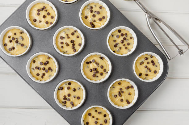 istock Raw dough for muffins with chocolate chips in baking form on a white wooden background. Recipe step by step. Top view. 1358754437