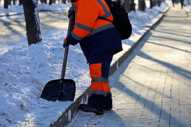 istock Worker in uniform with a shovel clears melting snow on a sidewalk 1358754562