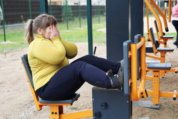 plump sad girl closed her face with hands, motivation of healthy lifestyle, sports street simulators - child obesity imagens e fotografias de stock