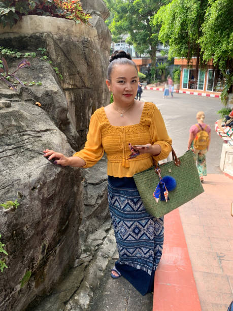 istock A woman wearing a yellow lace-patterned shirt and a Thai-patterned sarong is playing on a mobile phone. 1358756952
