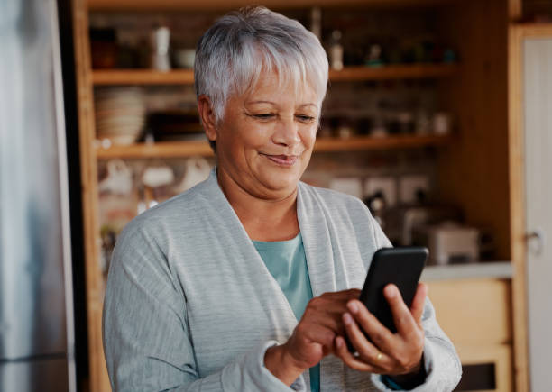 istock Smiling multi-cultural elderly female scrolling internet on smartphone while standing in modern kitchen 1358757395