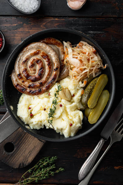 salsichas nürnberger alemãs fritas com chucrute, purê de batatas em frigideira de ferro fundido, em fundo de mesa de madeira escura velha - german culture salad prepared potato bratwurst - fotografias e filmes do acervo